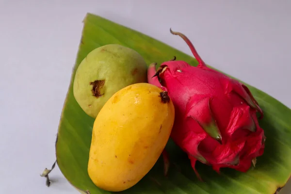 Beyaz arka planda izole edilmiş muz yaprağında ejderha meyvesi, mango ve guava..