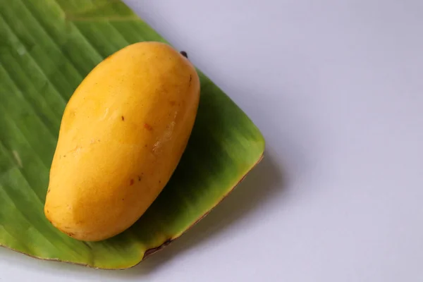 Muz yaprağında olgun sarı mango meyvesi, beyaz arka planda doğal yiyecek, yakın plan fotoğrafı..