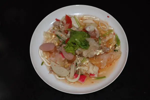 Tayland baharatlı yosunlu erişte salatası, sosisli ve sebzeli, siyah arka planda beyaz tabakta..