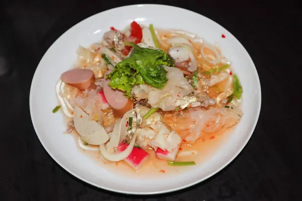 Tayland baharatlı yosunlu erişte salatası, sosisli ve sebzeli, siyah arka planda beyaz tabakta..