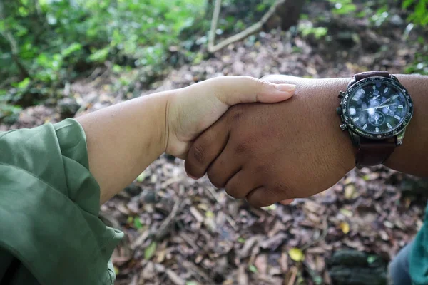 Male hand wearing watch holding hands with woman in forest