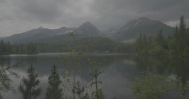 Tatra Dağları 'ndaki göl Strbskie Pleso. Sisli dağlarda, filmler dingin gölleri tasvir eder. Bulutlu gökyüzü kasvetli bir atmosfer yaratıyor. Yansımalar dalgalanır, sahneye ruhani bir cazibe katar. Doğanın güzelliği bulutlar tarafından engellenmeden parlıyor.