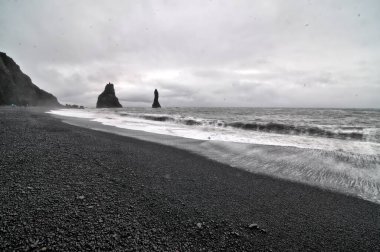 Reynisfjara 'nın dünyaca ünlü kara kumlu plajı İzlanda' nın güney kıyısında, bazalt sütunları ve dramatik Reynisdrangar deniz yığınlarıyla bulundu..
