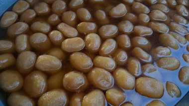 Yakın planda, açık altın-kahverengi renkli, şekerli şuruba batırılmış sayısız küçük, tatlı, süngerimsi toplar görülüyor..