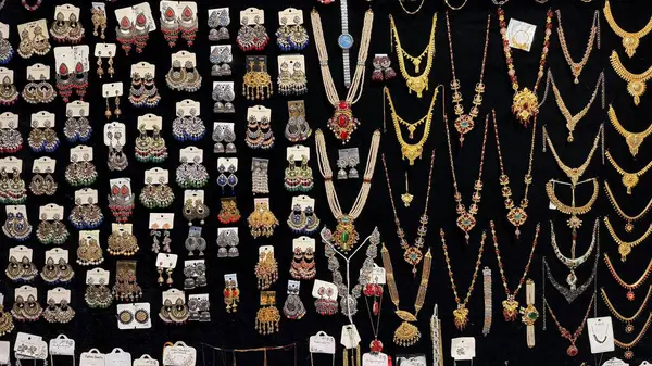 Bu resimde, koyu bir zemin üzerine yerleştirilmiş süslü Hint küpe ve kolyelerinden oluşan bir çeşitlilik sergilenmekte ve satılık kültürel mücevherlerin zengin bir görüntüsünü sunmaktadır..