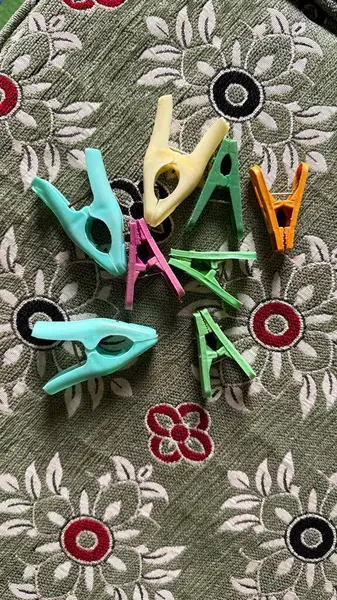 Göz hizasında, tam kare, canlı renkli plastik mandalları, narin beyaz ve kırmızı çiçekli desenli zeytin yeşili bir kumaşa serpiştirir ve neşeli bir doku oluşturur..