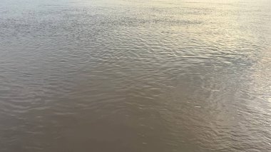 Güneş ışığı sakin nehir yüzeyinde dans ederek büyüleyici bir ışık ve gölge deseni oluşturur. Suyun hafif dalgaları, dinginliği ve doğal atmosferi arttırır..