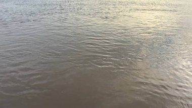 Nehrin sakin yüzeyini hafif dalgalanmalarla ve güneş ışığının ince yansımalarıyla yakalar. Suyun çerçeve boyunca akışını vurgular..