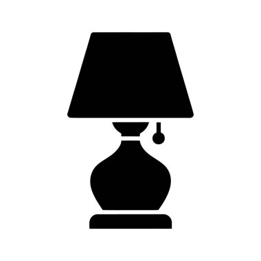 Siluet, klasik bir abajur tasarımı içeren bir masa lambasını tasvir eder. Zarif, soğanlı bir taban üzerinde beyaz arka planda görünür bir zincir anahtarı ile çekilir..