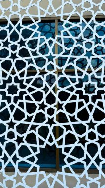Bu yüksek çözünürlüklü fotoğrafta beyaz İslami yıldız deseni mavi pencere çerçevelerini örtüyor ve geometrik simetri sanatı yaratıyor..