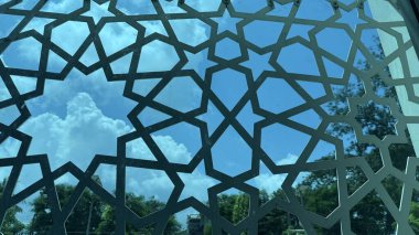 Süslü yıldız tasarımı, kabarık beyaz bulutlarla canlı mavi gökyüzünü çerçeveler. Çerçevenin arkasında ağaçlar ve binalar görülebilir. yüksek çözünürlük fotoğrafı.