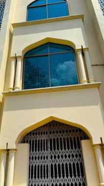 Yukarıdan bakıldığında gökyüzünü yansıtan kemerli camlı bej bir binanın mimari cephesi ve zemin katlanmış metal bir kapı görülüyor. Yüksek çözünürlüklü fotoğraf.