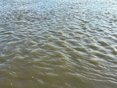 Tam kare yüksek çözünürlüklü fotoğraf dalgaları bulanık suyu yansıtıyor güneş ışığını yansıtıyor, suyun yüzeyinde karmaşık dalga desenleri yaratıyor, dinamik bir dokuyla sonuçlanıyor..