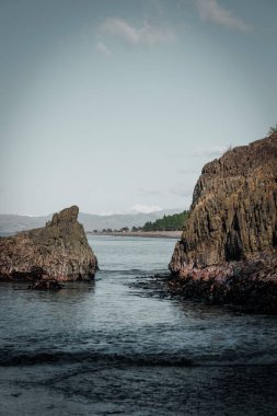 Yeni Zelanda 'daki Maymun Körfezi' nden bir fotoğraf. Çekim uzaktaki karlı bir dağı gösteriyor. Ön planda okyanus ve dağı çevreleyen iki kaya var.