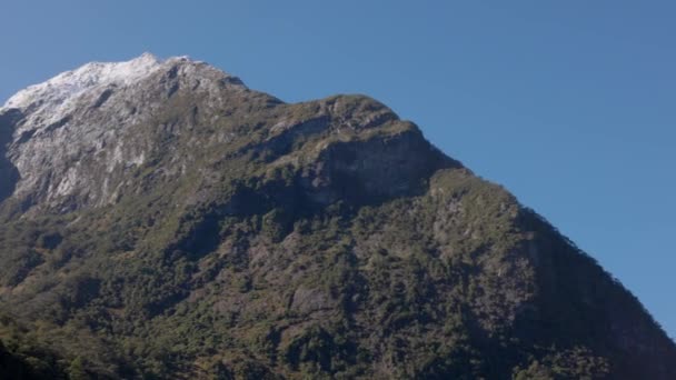 その上に雪が降る山脈のパンニングショット 撮影はニュージーランドのミルフォード サウンドで行われた — ストック動画