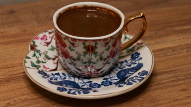 Köpüklü kahveyle dolu parlak gri bir kahve fincanı, arka plandaki cam pencere duvarına bağlı ahşap bir tahta, güpegündüz çekilmiş..