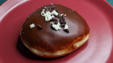 Üstünde çikolata sosu olan taze bir çörek ve kırmızı tabakta servis edilen siyah ve beyaz çikolata parçaları..