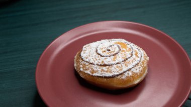 Üzerinde pudra şekeri ve yuvarlak çikolata sosu olan taze bir çörek, kırmızı tabakta servis edilir..