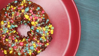 Kırmızı bir tabakta servis edilen büyük renkli şekerli taze çikolata soslu donut..