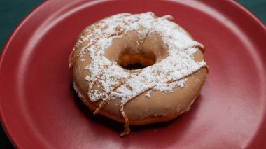Üzerine karamel sosu serpiştirilmiş taze bir çörek ve pudra şekeri, kırmızı bir tabakta servis edilir..