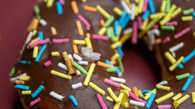 Üzerinde renkli şekerler olan çikolata soslu bir çörek, kırmızı bir tabağa konmuş..