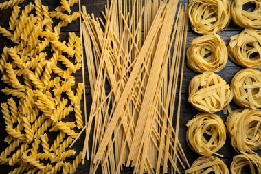 Makarna şekilleri, spagetti, fusilli, tagliatelle, ahşap arka planda İtalyan mutfağı malzemeleri.