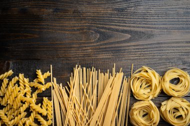 Makarna şekilleri, spagetti, fusilli, tagliatelle, ahşap arka planda İtalyan mutfağı malzemeleri.