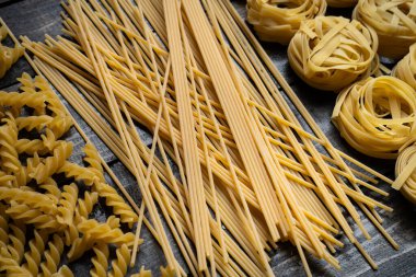 Makarna şekilleri, spagetti, fusilli, tagliatelle, ahşap arka planda İtalyan mutfağı malzemeleri.