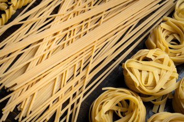 Makarna şekilleri, spagetti ve tagliatelle, ahşap arka planda İtalyan mutfağı malzemeleri.
