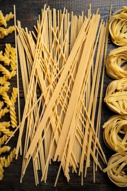 Makarna şekilleri, spagetti, fusilli, tagliatelle, ahşap arka planda İtalyan mutfağı malzemeleri.