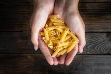 Çiğ İtalyan makarna makarna iki elle tutulan koyu ahşap arka plan