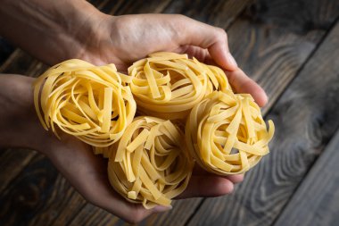 Çiğ İtalyan makarna tagliatelle iki elle tutulmuş koyu ahşap bir arka plan üzerinde