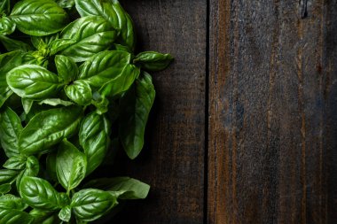 Koyu ahşap arka planda taze organik fesleğen yaprakları.