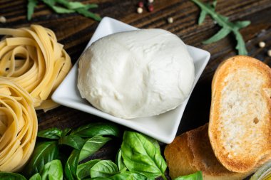 İtalyan yemek malzemeleri, taze mozzarella, bruschetta, çiğ tagliatelle ve koyu ahşap arka planda fesleğen yaprakları.