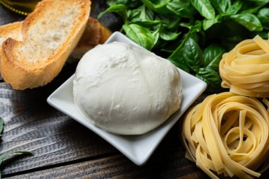 İtalyan yemek malzemeleri, taze mozzarella, bruschetta, çiğ tagliatelle ve koyu ahşap arka planda fesleğen yaprakları.
