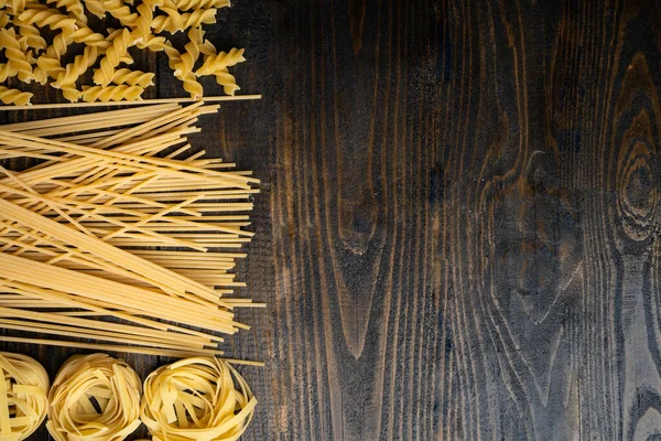 Makarna şekilleri, spagetti, fusilli, tagliatelle, ahşap arka planda İtalyan mutfağı malzemeleri.