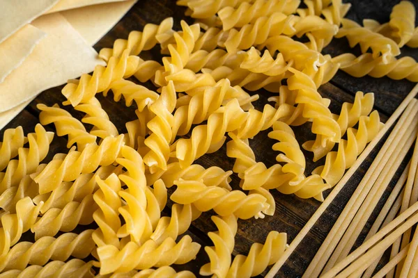 Makarna şekilleri, spagetti, fusilli, lazanya, ahşap arka planda çiğ İtalyan mutfağı malzemeleri.