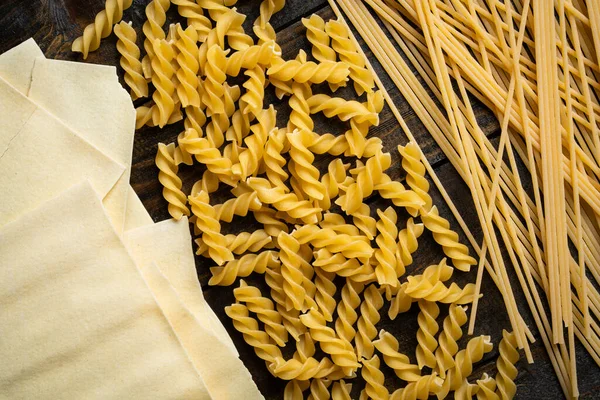 Makarna şekilleri, spagetti, fusilli, lazanya, ahşap arka planda İtalyan mutfağı malzemeleri.