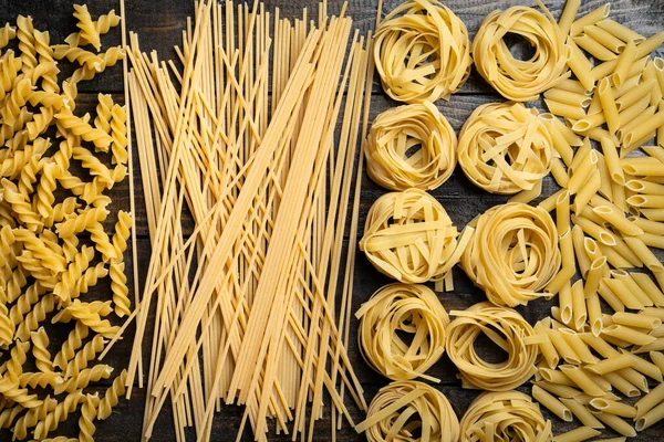 Makarna şekilleri, çiğ spagetti, fusilli, tagliatelle ve makarna, ahşap arka planda İtalyan mutfağı malzemeleri.