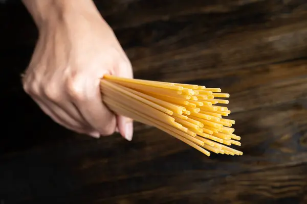 Çiğ İtalyan makarna tagliatelle 'i koyu ahşap bir arka planda tutuyordu.