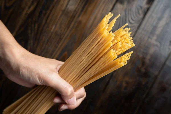 Çiğ İtalyan makarna tagliatelle 'i koyu ahşap bir arka planda tutuyordu.