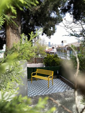 Bankta, evin verandasındaki sarı bankın dikey fotoğrafı ağaçların arasından görülüyor, uzaktan çekilmiş. Gürültü, Seçici Odaklanma