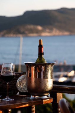 Deniz manzaralı romantizmin dikey fotoğrafı. Öğleden sonra masada deniz manzaralı bir şişe şarap ve şarap kadehi. Seçici Odaklanma.