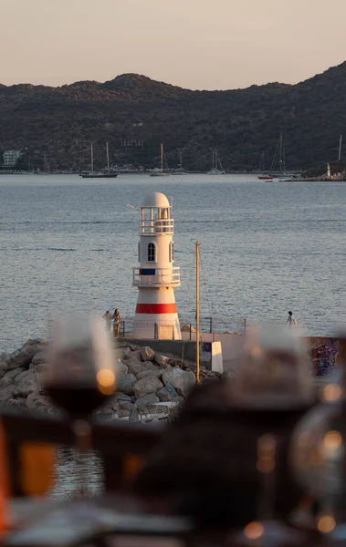 Deniz feneri. Deniz fenerinin dikey fotoğrafı. Öğleden sonra masada deniz manzaralı iki şarap kadehi. Seçici Odaklanma.