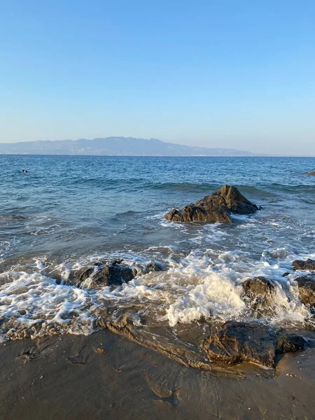 Kabaran dalgalar, güneşli ve rüzgarlı bir yaz gününde deniz kayalarında kabaran dalgaların dikey fotoğrafı.