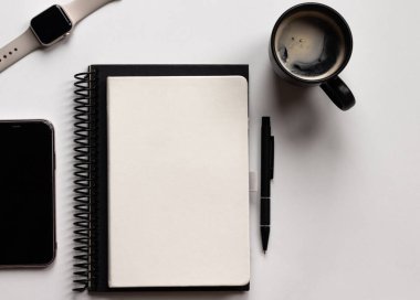 Not defterleri, kalem, akıllı telefon, akıllı gözlük ve kahve fincanı olan modern beyaz ofis masası. Ortadaki metin girişi için boş defter sayfası. Üst manzara, düz uzanma.