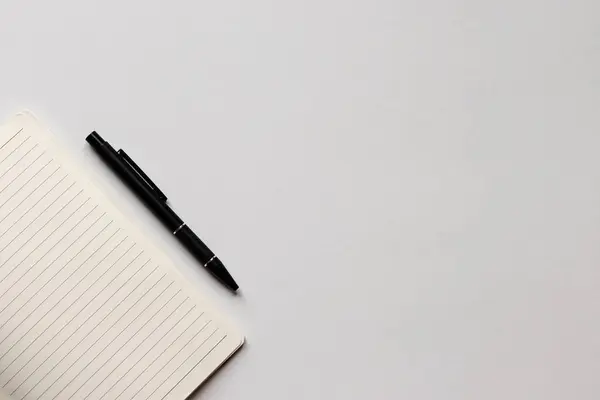Kısmi çizgili bir defter ve beyaz ofis masasında bir kalem. Minimalizm, düz uzanma. 