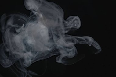 Duman ve buhar rüzgarda uçuşuyor. Siyah arka planın önünde.