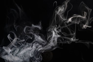 Duman ve buhar rüzgarda uçuşuyor. Siyah arka planın önünde.