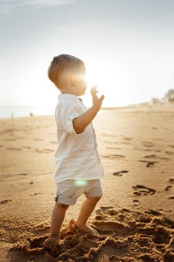 Çocuk gün batımında sahilde yürüyor..